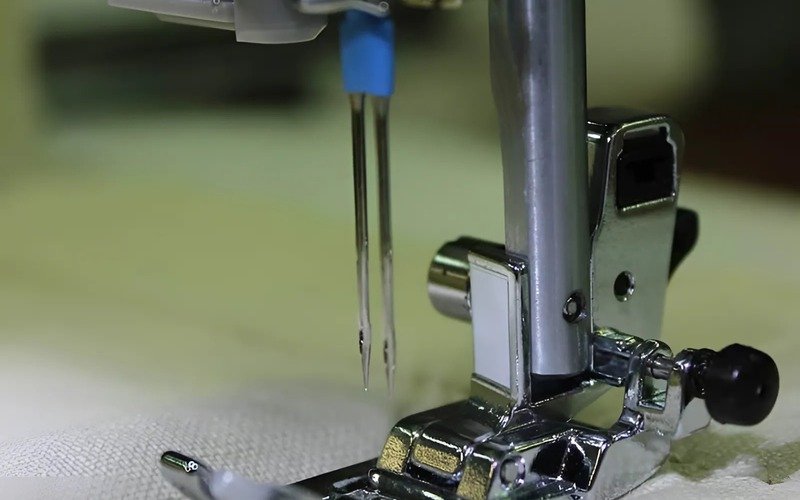 Twin needles on a sewing machine are used to sew two parallel rows of stitches at the same time